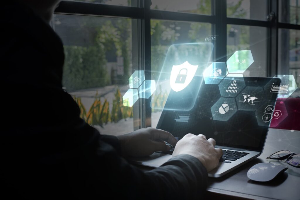 A woman types on her laptop while a blue graphic of cyber security images glows from the laptop screen