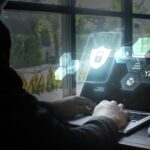 A woman types on her laptop while a blue graphic of cyber security images glows from the laptop screen