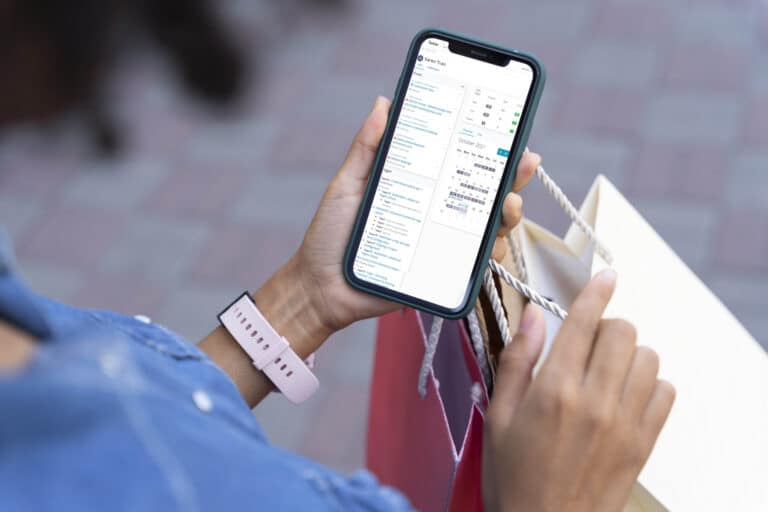 A woman holds a few shopping bags and her smartphone, showing the Tackler custom software app on mobile.