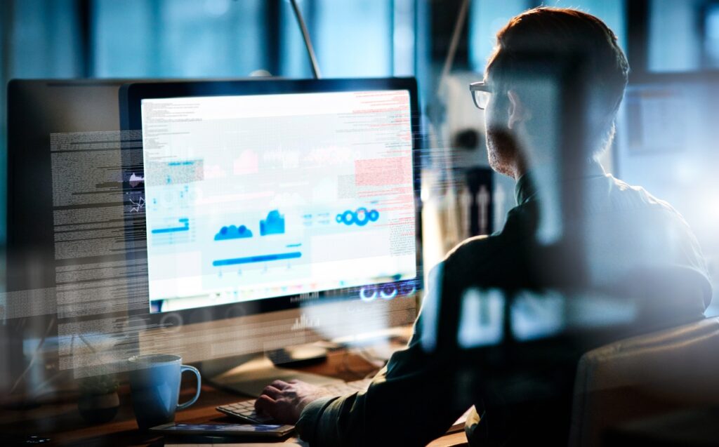 A man in glasses sits at a computer desk and works on a computer problem