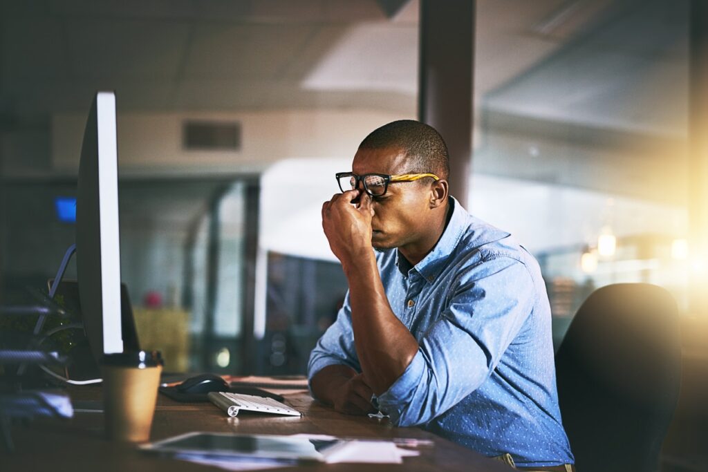 A young office worker sits at his computer desk, scrunching his face in frustration.