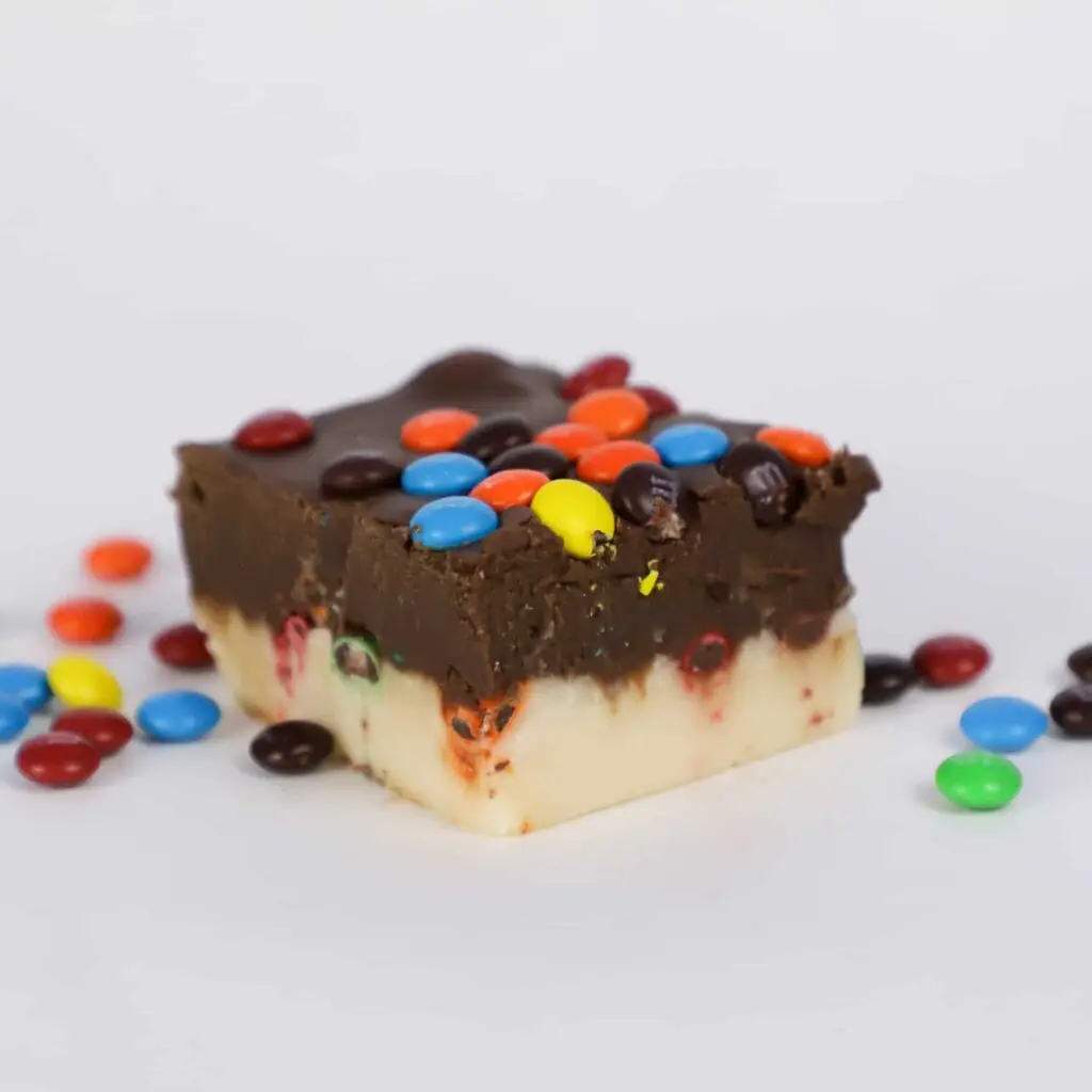 Mini chocolate M&M candies sandwiches between a layer of vanilla and chocolate fudge, then topping the portion of fudge and sprinkling the surroundings as well.