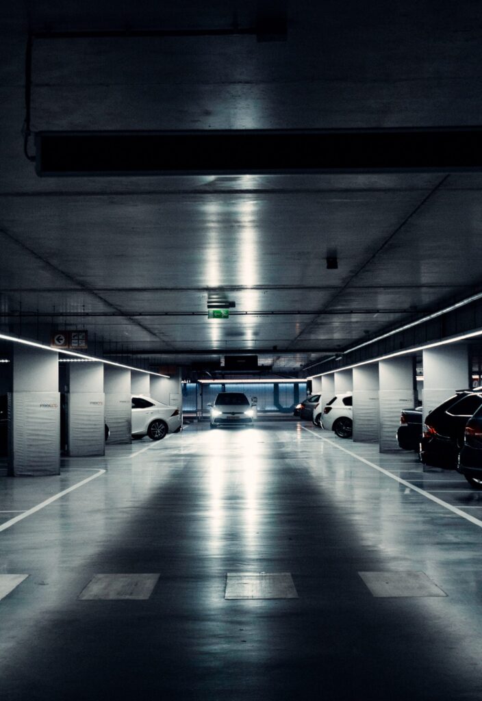 car with headlights in a covered parking garage with other cars parked in parking spaces